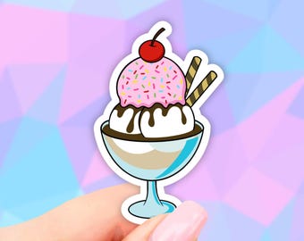 May include: A cartoon illustration of a pink and white ice cream sundae with chocolate sauce and two wafer cookies in a clear glass dish.