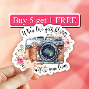 May include: A sticker with a vintage camera and floral design. The text reads "When life gets blurry adjust your focus".