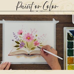 May include: A watercolor painting on paper featuring an open book with pink and purple flowers emerging from the pages. The artwork includes green leaves and delicate floral stems. A paintbrush is held near the paper, with a paint palette nearby.
