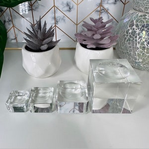 May include: Four clear glass display stands of varying sizes, perfect for showcasing small items like jewelry or crystals. The stands are square and have a raised platform in the center.