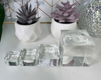 May include: Four clear glass display stands of varying sizes, perfect for showcasing small items like jewelry or crystals. The stands are square and have a raised platform in the center.