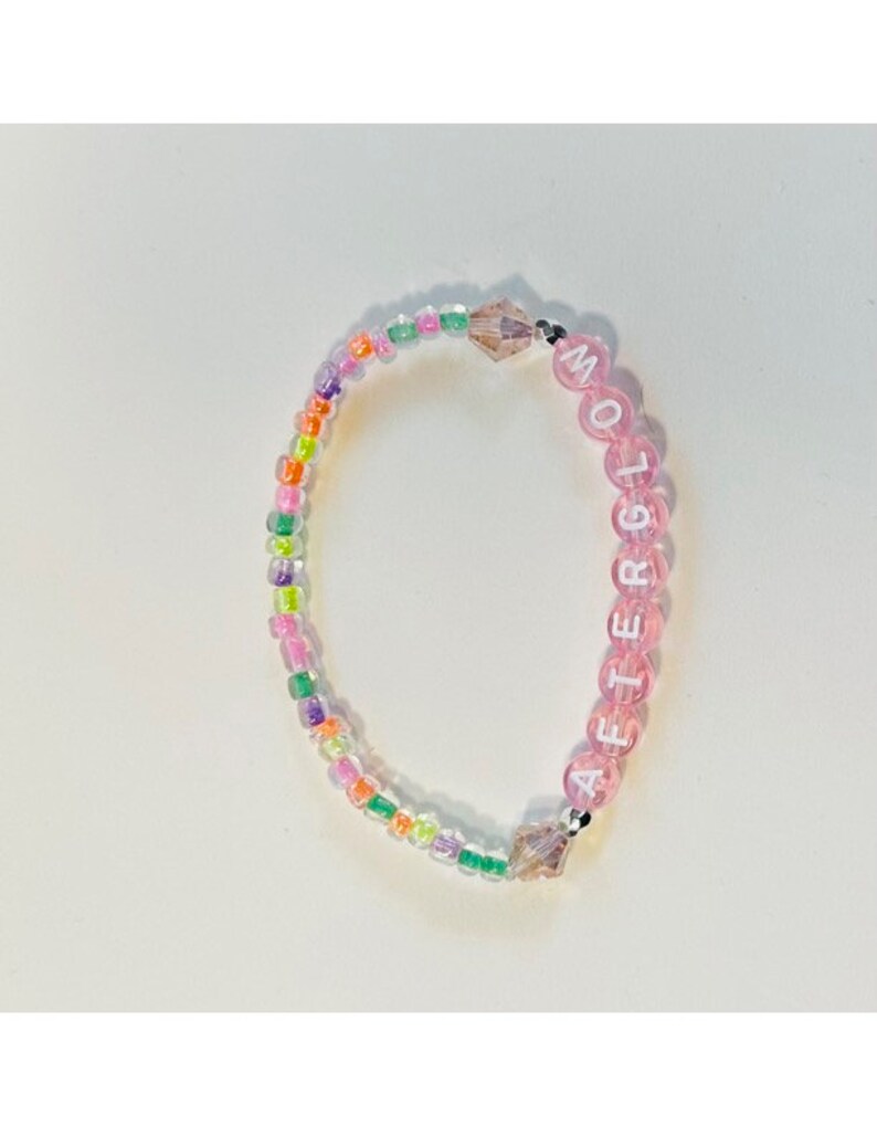 May include: A pink beaded bracelet with the word "AFTERGLOW" spelled out in white letters. The beads are interspersed with small, iridescent, multi-colored beads.