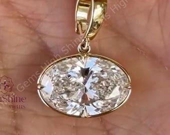 May include: A gold pendant with an oval-cut diamond. The diamond is set in a gold bezel and has a brilliant sparkle. The pendant has a simple, elegant design, perfect for everyday wear. The pendant is held in a hand.
