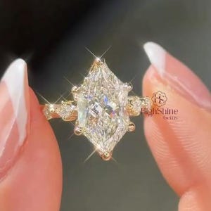May include: A gold ring featuring a large marquise-cut center diamond held by prongs, flanked by smaller round accent diamonds on each side of the band. The ring displays the text HighShine Gems in a small logo on the right side of the setting.