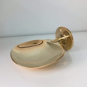 Peut inclure: Un porte-savon mural doré. Le porte-savon a une forme arrondie en forme de coquillage avec un design à charnière. Il est fixé à une base circulaire avec des trous de vis pour le montage. Le porte-savon est en métal brillant.