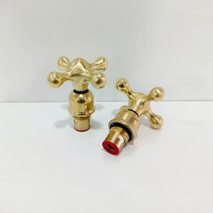 Peut inclure: Deux poignées de robinet de couleur dorée avec des boutons en forme de croix. Les poignées ont une rondelle en caoutchouc rouge au bas.