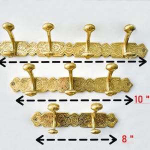 Puede incluir: Tres percheros de latón con diseños ornamentados. El perchero superior mide 16 pulgadas de largo, el del medio 10 pulgadas y el inferior 8 pulgadas.