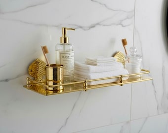 May include: A gold-toned bathroom shelf with a soap dispenser, toothbrush, and a small gold fish-shaped decoration. The shelf also holds a stack of white towels and a glass jar with cotton balls.