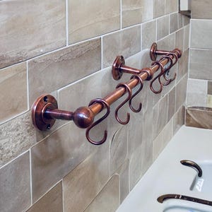 Peut inclure: Un porte-serviettes en métal de couleur cuivre avec six crochets incurvés. Le porte-serviettes est monté sur un mur carrelé. Le porte-serviettes a une boule ronde à l'extrémité et est fixé au mur avec des plaques rondes.