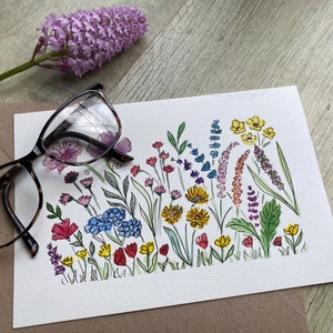 May include: A watercolor painting of a colorful bouquet of flowers. The flowers are painted in shades of pink, purple, blue, yellow, and green. The painting is on a white background.