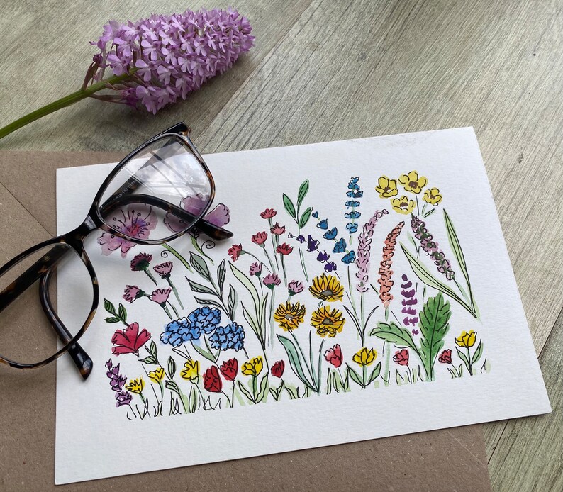 May include: A watercolor painting of a colorful bouquet of flowers. The flowers are painted in shades of pink, purple, blue, yellow, and green. The painting is on a white background.