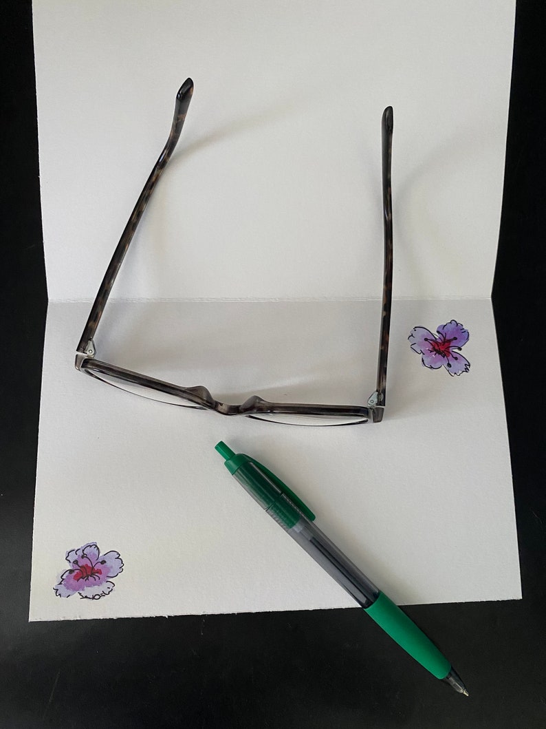 May include: A white card with a green pen, a pair of tortoiseshell glasses, and two purple flowers drawn on it.