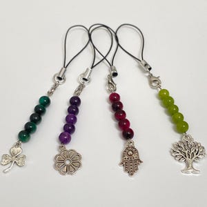 Op de afbeelding: Vier bedelarmbanden met zilverkleurige metalen accenten. Elke bedel heeft een andere kleur kralen: groen, paars, rood en geelgroen. Bedels zijn onder meer een klavertjevier, een bloem, een Hamsa-hand en een boom.