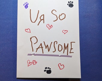 May include: A white card with the words "Ur so Pawsome" written in brown marker. The card is decorated with purple and black paw prints and red hearts.