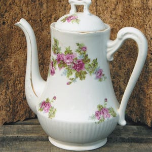 Vintage keramische koffiepot met roze bloemversiering.