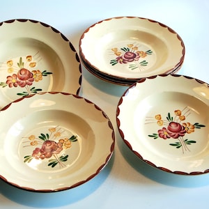 May include: A collection of cream-coloured ceramic bowls with scalloped brown edges. Each bowl displays a hand-painted floral design in red, yellow, and green. The bowls are arranged on a light blue surface.