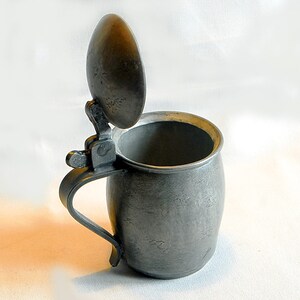 May include: A pewter tankard with a hinged lid. The tankard has a rounded body and a handle. The lid is open and the inside of the tankard is visible.
