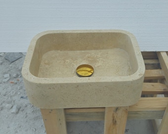 May include: A rectangular stone sink with a rounded edge and a gold drain cover. The sink is sitting on a wooden stand.