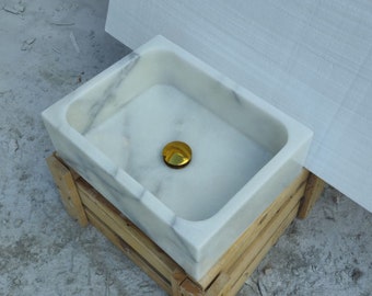 May include: A white marble sink with a gold drain stopper. The sink is sitting on a wooden crate.