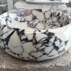 May include: A white marble bowl with black and purple veining. The bowl is round and has a smooth, polished finish.