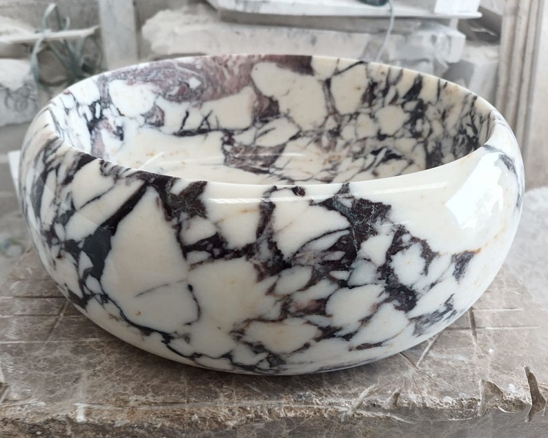 May include: A white marble bowl with black and purple veining. The bowl is round and has a smooth, polished finish.
