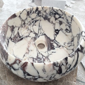 May include: A white marble sink with a round shape and a purple and black marbling pattern.