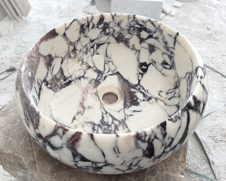 May include: A white marble sink with a round shape and a purple and black marbling pattern.