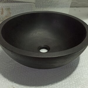 May include: A black round ceramic sink with a smooth, slightly textured surface. The sink has a small drain hole in the center.