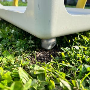 K&ouml;nnte beinhalten: Nahaufnahme eines wei&szlig;en Tisches mit einem silbernen Laufrollenrad auf einem Bett aus gr&uuml;nem Gras.