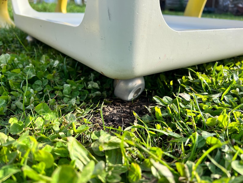K&ouml;nnte beinhalten: Nahaufnahme eines wei&szlig;en Tisches mit einem silbernen Laufrollenrad auf einem Bett aus gr&uuml;nem Gras.