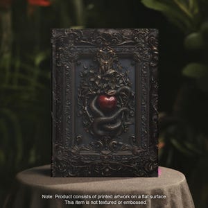 May include: A black framed print of a snake wrapped around a red apple. The snake and apple are in a 3D style, appearing to be sculpted. The print is set against a dark background.