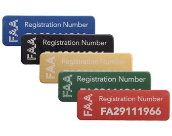 Puede incluir: Cinco etiquetas rectangulares de metal con el texto "FAA Registration Number" y un número de registro. Las etiquetas son de color azul, negro, dorado, verde y rojo.