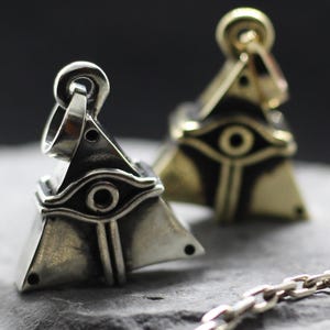 May include: Two silver pyramid pendants with an eye design. The pendants are on a silver chain.