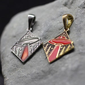 May include: Two diamond-shaped metal pendants featuring an engraved UFO scene with a tractor beam over a forest. One pendant is silver-toned with a dark red beam, and the other is gold-toned with a bright red enamel beam and black accents.