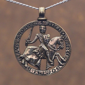 May include: A silver-coloured pendant necklace. The circular pendant depicts a knight on horseback, holding a sword. The knight is in armour. The pendant has an ornate border with text. The necklace chain is silver.