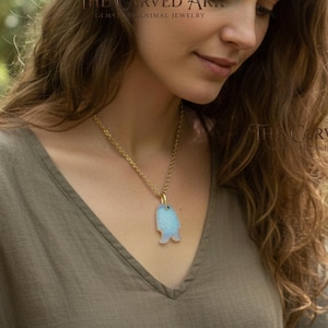 May include: A gold-colored chain necklace with a light blue fish pendant. The pendant has a unique shape and is suspended from a delicate chain. The necklace is a piece of animal jewelry.