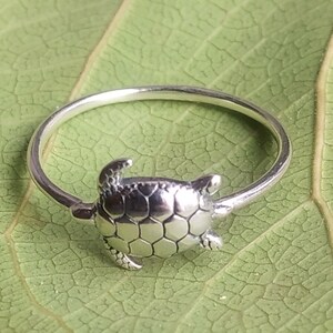 Op de afbeelding: Een zilveren ring met een schildpadontwerp. De schildpad is gedetailleerd met een getextureerde schild en heeft een eenvoudige band.