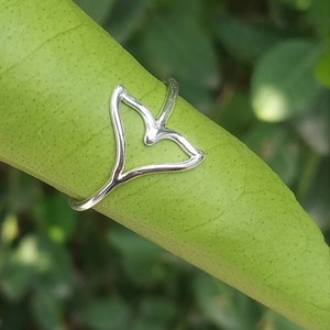May include: A silver ring featuring a whale tail design. The ring is resting on a green leaf.