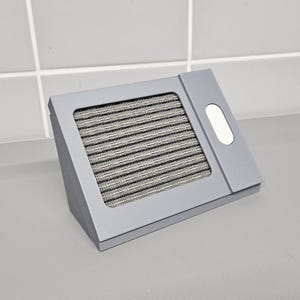 May include: A gray, rectangular speaker with a black speaker grille and a small, white button on the side.