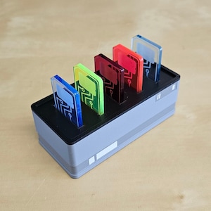 Pode incluir: Um organizador cinza e preto com cinco ranhuras contém cinco cartões de plástico transparente com desenhos de placas de circuito. Os cartões são de diferentes cores: azul, verde, amarelo, vermelho e azul claro.