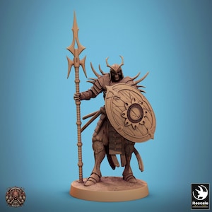 May include: A detailed figurine of a warrior with a spear and shield. The figure is brown with intricate armor, a horned helmet, and a shield with a sunburst design. The warrior stands on a circular base, with a light blue background.