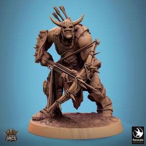 May include: A brown, sculpted miniature of an Orc warrior holding a crossbow. The Orc is wearing armor and has a fierce expression on its face. The miniature is set on a brown base.