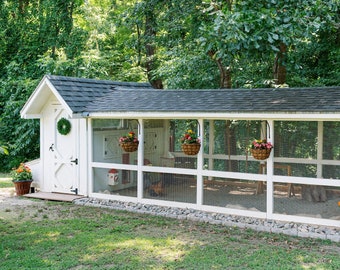 May include: White chicken coop with a screened-in run. The coop has a black shingled roof and a white door with a green wreath. There are hanging flower baskets on the front of the coop.