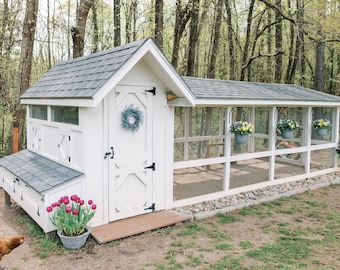 Puede incluir: Un gallinero de madera blanca con techo de tejas gris oscuro, una puerta central con una corona azul y un recinto de malla metálica adjunto. La estructura cuenta con macetas colgantes, un área de nido y una gallina marrón cerca.
