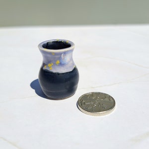 Könnte beinhalten: Handgefertigte Miniatur-Keramikvase mit dunkelblauem Boden und hellblau-gelb gesprenkelter Oberseite. Die Vase ist etwa 5 cm hoch. Eine Münze liegt daneben zum Größenvergleich.