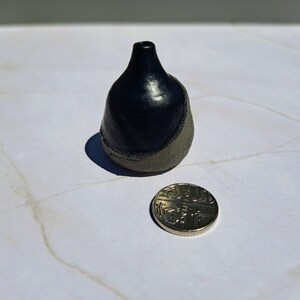 Puede incluir: Un pequeño jarrón de cerámica azul oscuro con un esmalte gris claro en la mitad inferior. El jarrón es aproximadamente del tamaño de una moneda de 20 céntimos de euro.