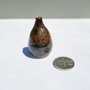 May include: A small, dark brown and blue ceramic vase with a speckled glaze. The vase is about the size of a UK 20 pence coin.