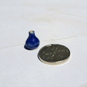 May include: A small blue ceramic vase with a rounded bottom and a narrow neck. The vase is about the size of a UK 20 pence coin.
