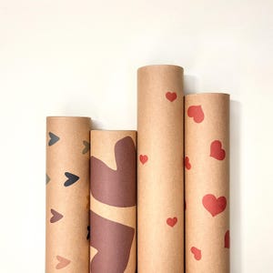 Vier Kraftpapier-Geschenkpapierrollen nebeneinander stehend mit verschiedenen Herzmustern – bunte Herzen, abstraktes Design, kleine rote Herzen und große rote Herzen, romantisches handgefertigtes Geschenkpapier aus hochwertigem Papier