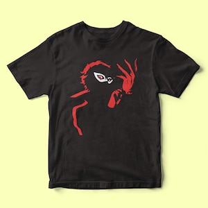 Peut inclure: T-shirt noir avec une silhouette rouge d'une figure masquée avec un seul œil visible.